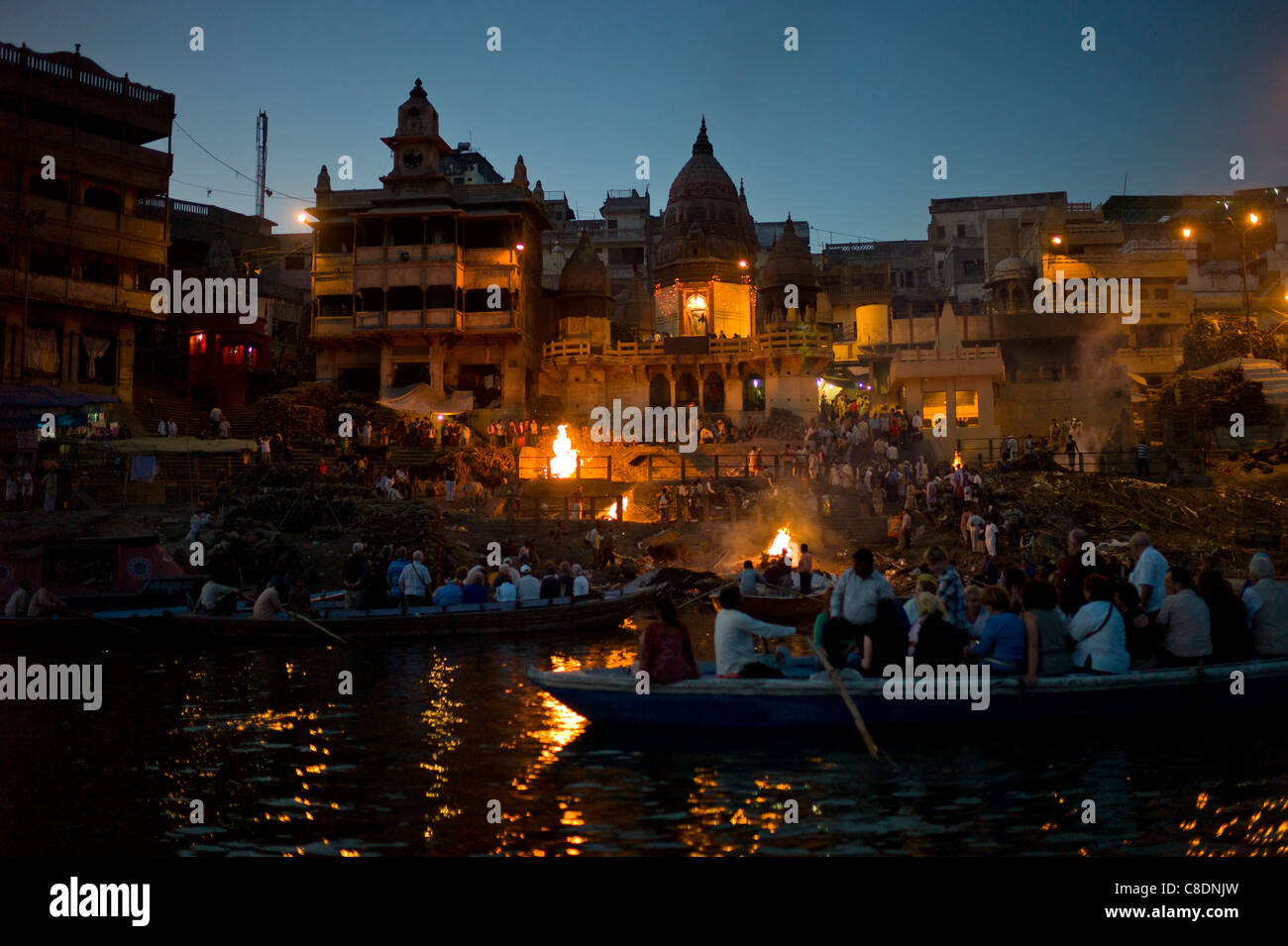 Touristen sehen Hindu Einäscherung auf Scheiterhaufen am Manikarnika Ghat, Fluss Ganges, in der Heiligen Stadt Varanasi, Benares, Indien Stockfoto