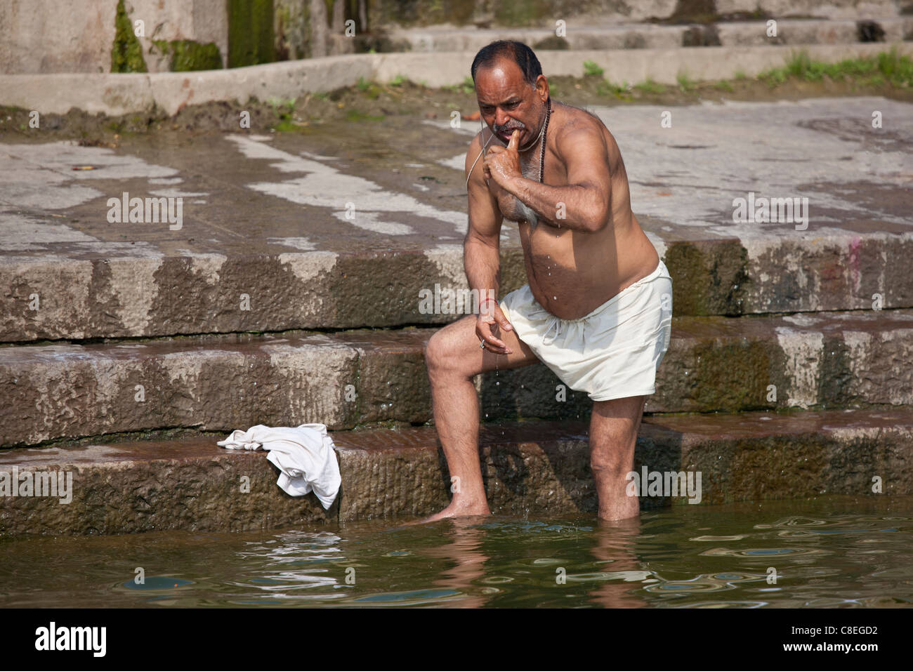 Indisch-hinduistischen Mann Baden und Reinigung seiner Zähne in den Fluss Ganges durch Kshameshwar Ghat in der Heiligen Stadt Varanasi, Indien Stockfoto