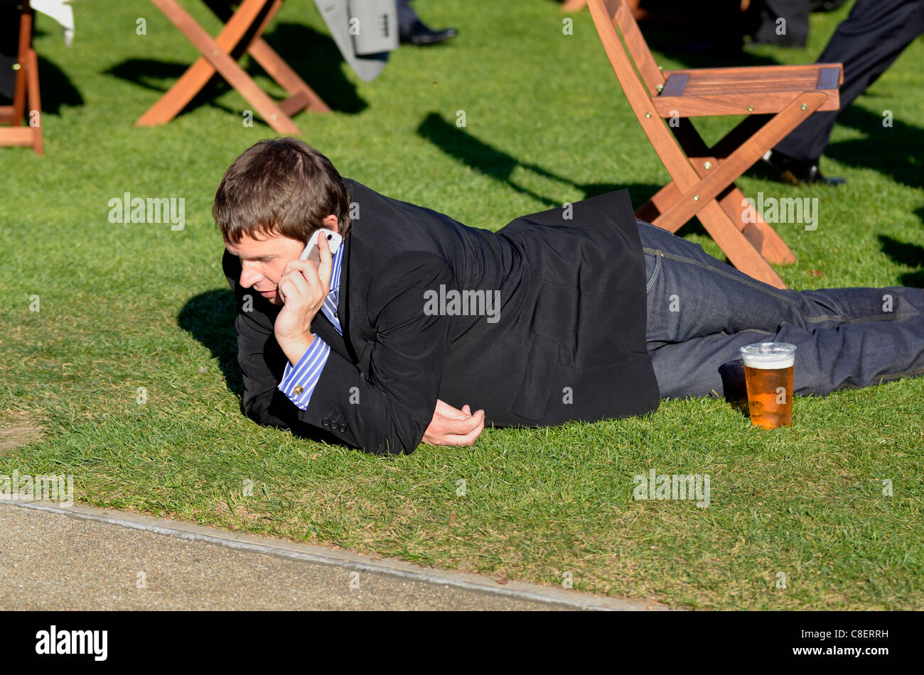 Mann mit mobilen beim liegen auf dem Rasen Ascot Rennen UK Stockfoto