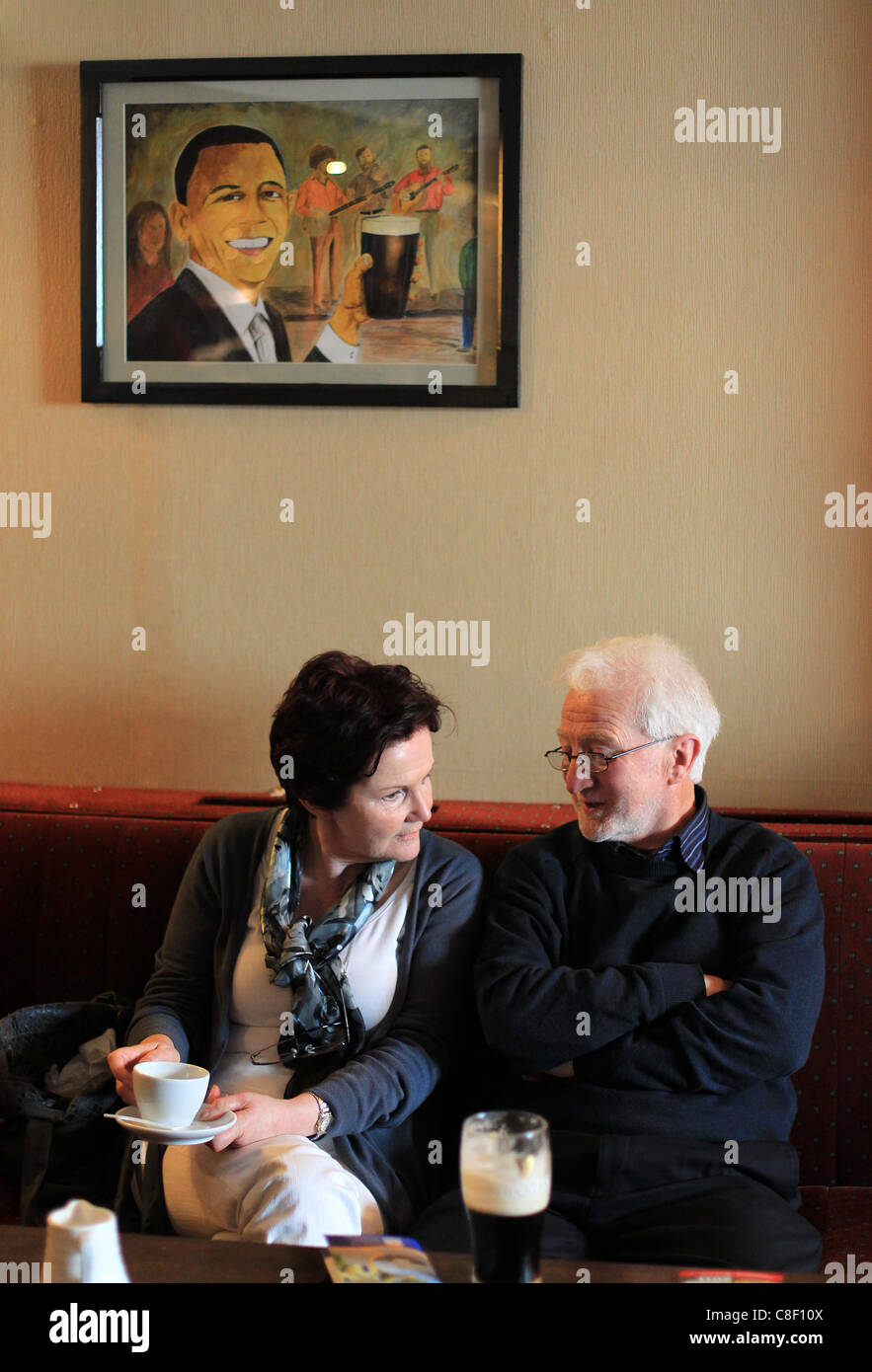Zwei ältere Leute genießen ein Bier und eine Tasse Tee als ein Bild der US-Präsident Barack Obama über ihnen in einem irischen Pub hängt Stockfoto