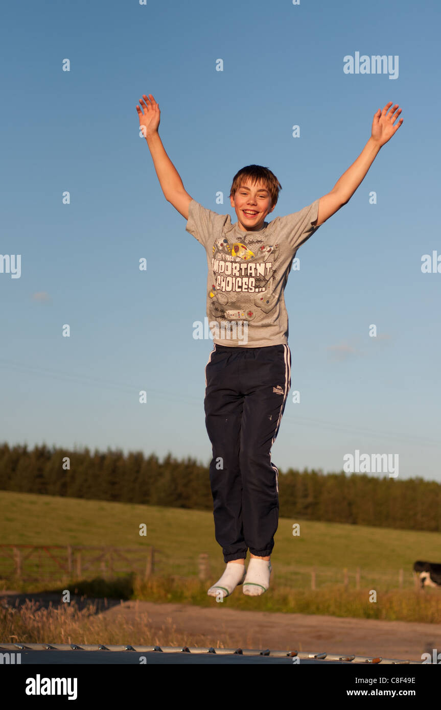 Teenager Prellen und lachend auf einem Trampolin mit seinen Armen in der Luft und trug ein graues T-Shirt, Trainingshose und Socken im Juli Stockfoto