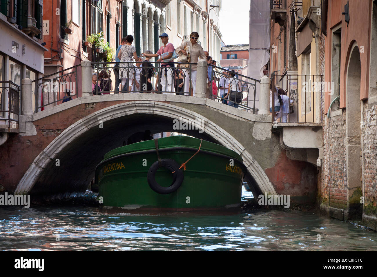 ein Lastkahn vorbei unter einer kleinen Brücke mit Touristen auf der Brücke in Venedig. Stockfoto