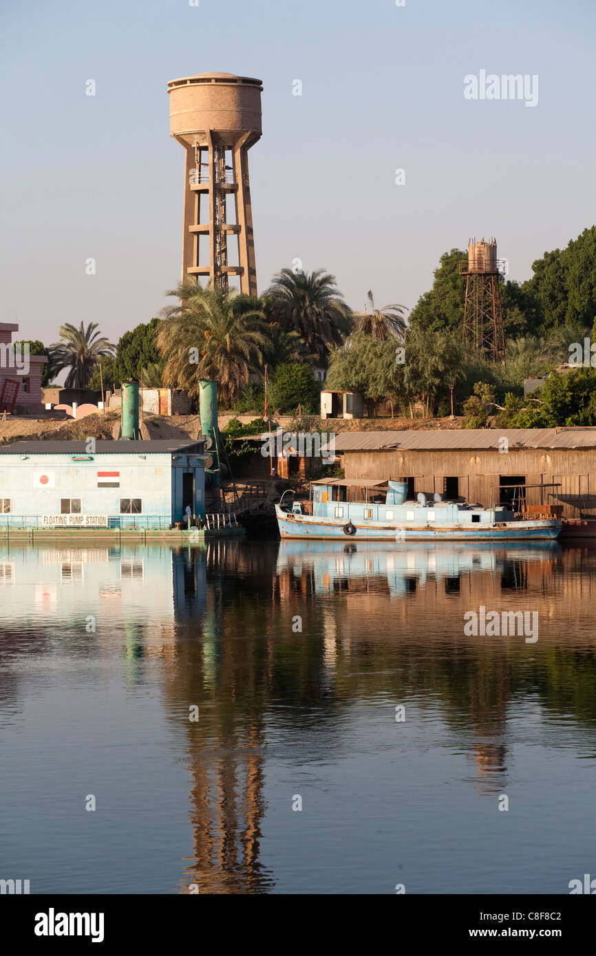 Nil-Ufer mit kleinen blauen, vereinzelt Spritztülle Boot ankern neben Schuppen, Pumpstation und Wasserturm auf der Rückseite Boden Stockfoto