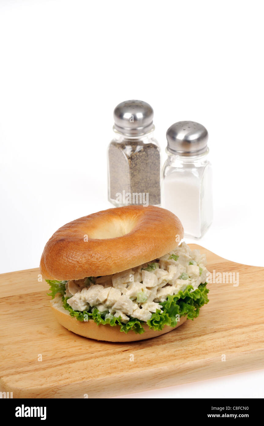 Hähnchen-Salat-Sandwich mit Salat in einem Bagel auf Holz Schneidebrett mit Salz & Pepper Shakers auf weißem Hintergrund. Stockfoto