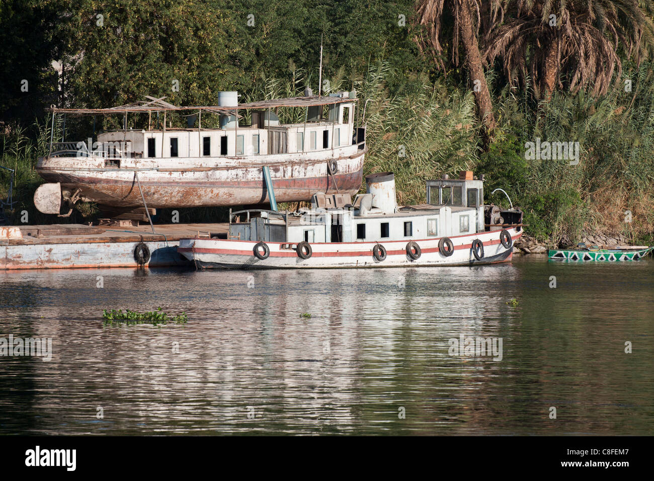 Ein Teil der Nil-Ufer mit altes Boot im Trockendock mit einem einzigen Trichter Boot ankern vor Rost im Wasser gespiegelt Stockfoto