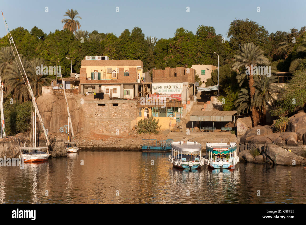 am späten Nachmittag Schuss Feluken und Wassertaxis vor Anker vor einem kleinen Dorf am Fluss Nil, spiegelt sich in ruhigem Wasser Stockfoto