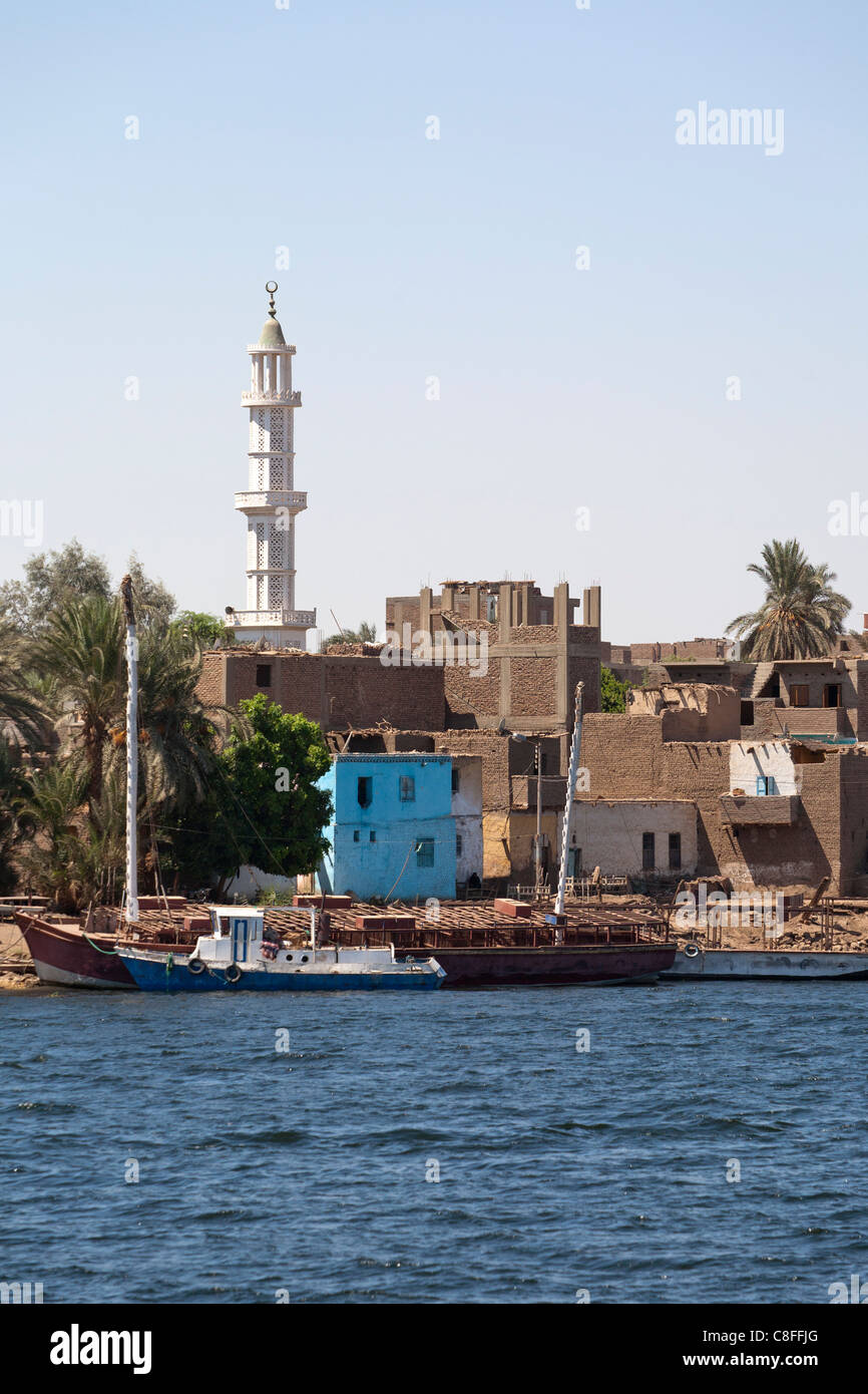 Ein Teil der Nil-Ufer mit zwei ankern Boote vor traditionellen Schlamm Backsteinhäuser und Minarett der Moschee im Hintergrund Stockfoto