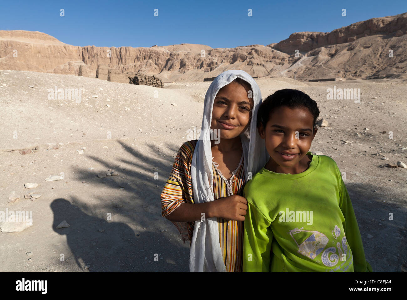 Zwei junge ägyptische Mädchen gerichtete Kamera tragen leuchtende Farben mit Wüste im Hintergrund, Luxor, Ägypten Stockfoto