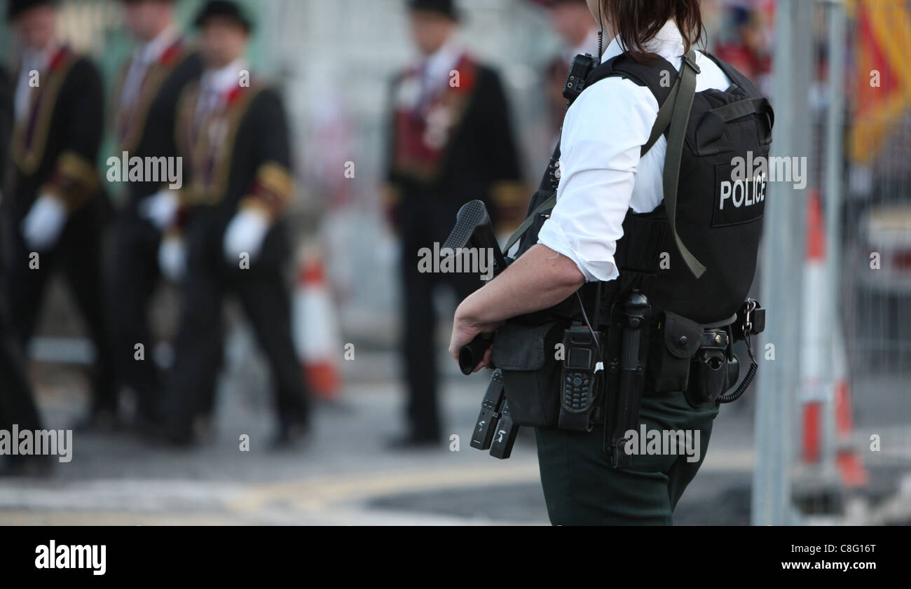 Ein Polizist wacht über eine Parade, wie sie eine Waffe trägt. Stockfoto