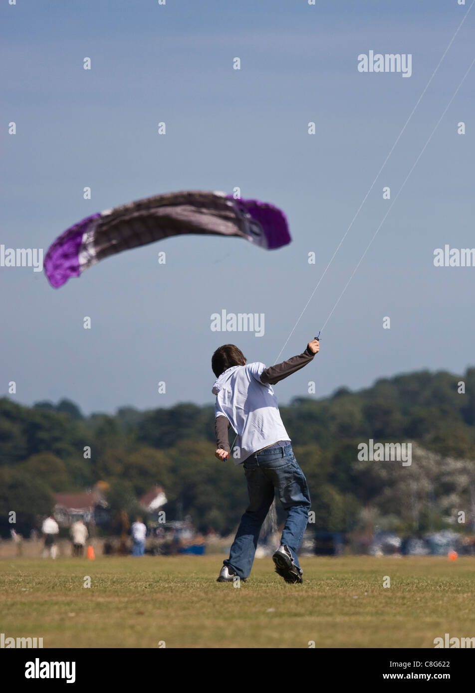 Ein Teenager kämpfen, um eine große sparless Drachenfliegen in der Sommersonne zu kontrollieren. Ein weiterer Drachen fliegt in das Foto. Stockfoto