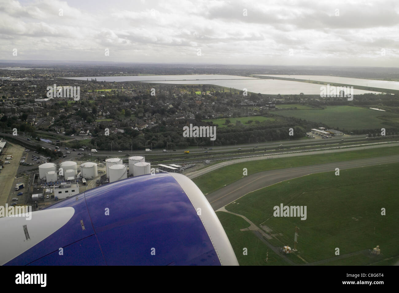 Blick vom Jet Flugzeug Beifahrerfenster an nehmen Sie ab mit Motor im Vordergrund und Land mit Feldern und Straßen unten Stockfoto