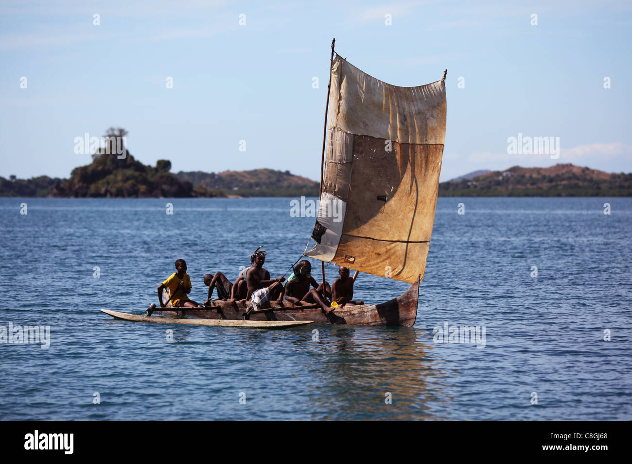 Eine traditionelle madagassische Piroge mit einem geflickten Segel zwischen Nosy Sakatia und Nosy Be, Madagaskar, mit mehreren jungen Fischer. Stockfoto