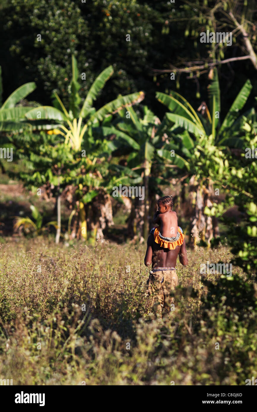Ein junger madagassischen Mann trägt eine Mädchen auf seinen Schultern zurück zu ihrer Hütte in der Mitte der Insel Nosy Sakatia, in der Nähe von Nosy Be Stockfoto