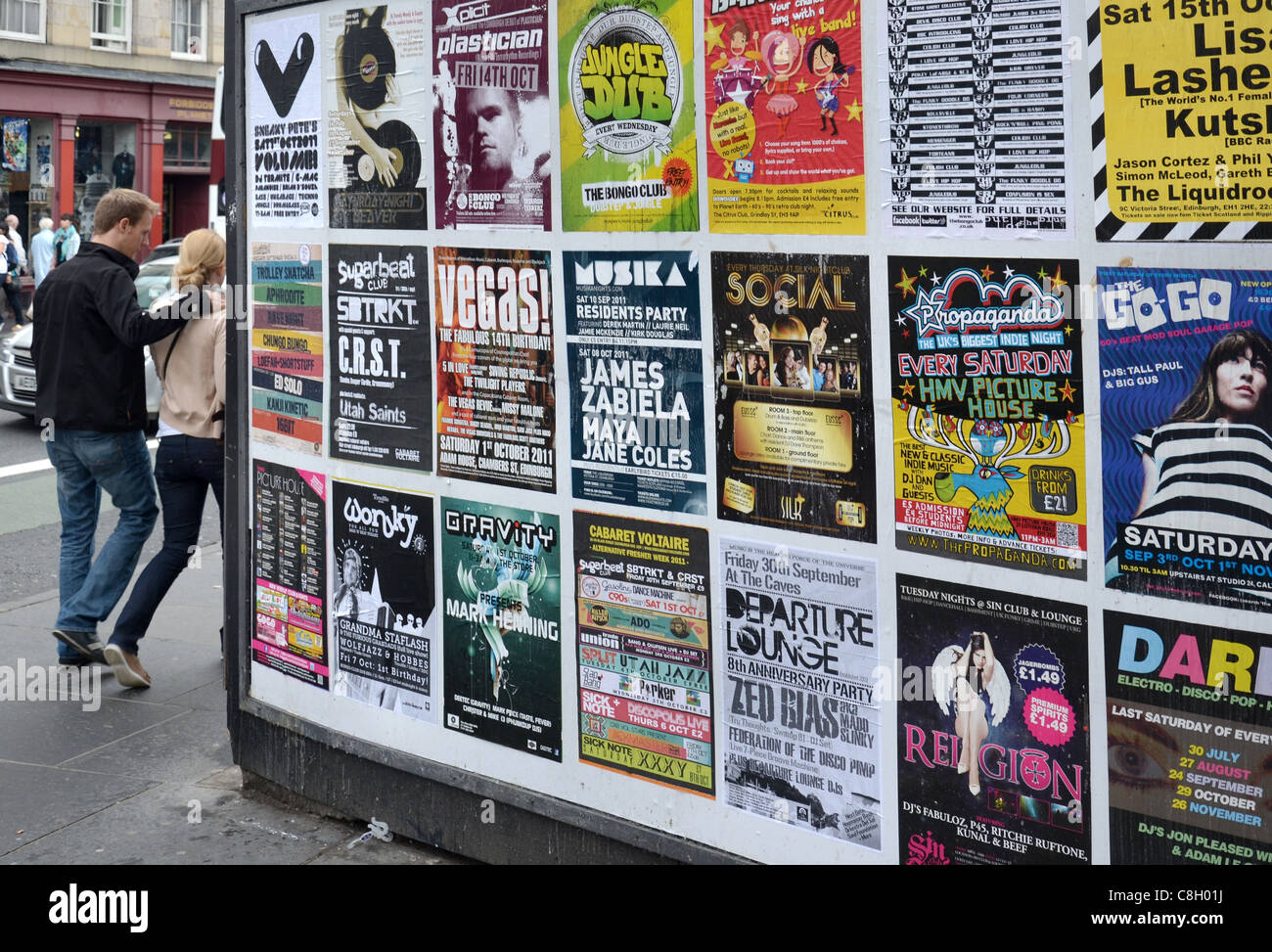 Ein junges Paar Fuß mit einer Plakatwerbung verschiedene Nachtclubs in Edinburgh. Stockfoto