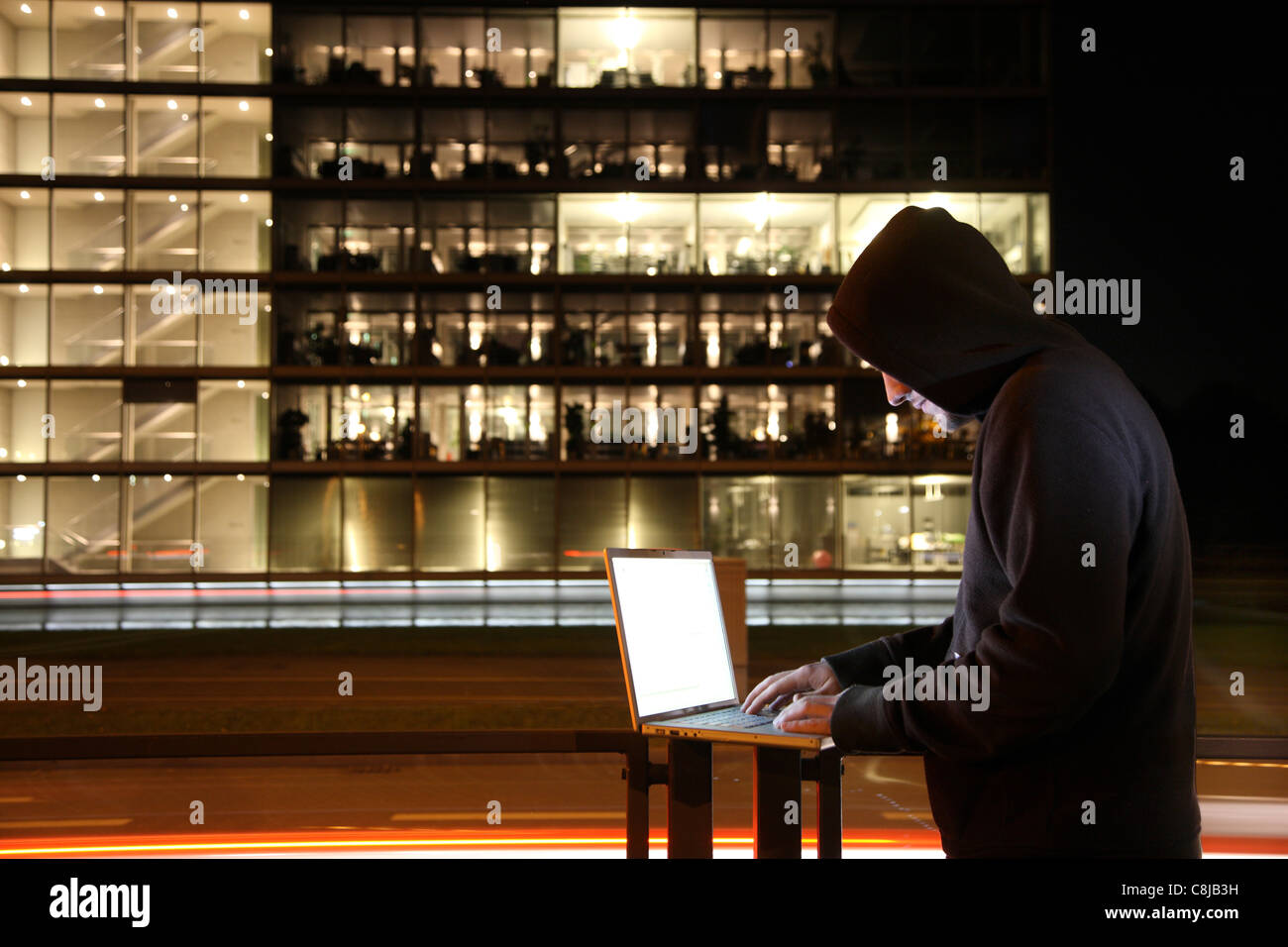 Computer-Benutzer, Hacker, verschwörerisch, sitzt außen vor einem Bürogebäude, mit einem Laptop. Symbolbild, Computer- Stockfoto