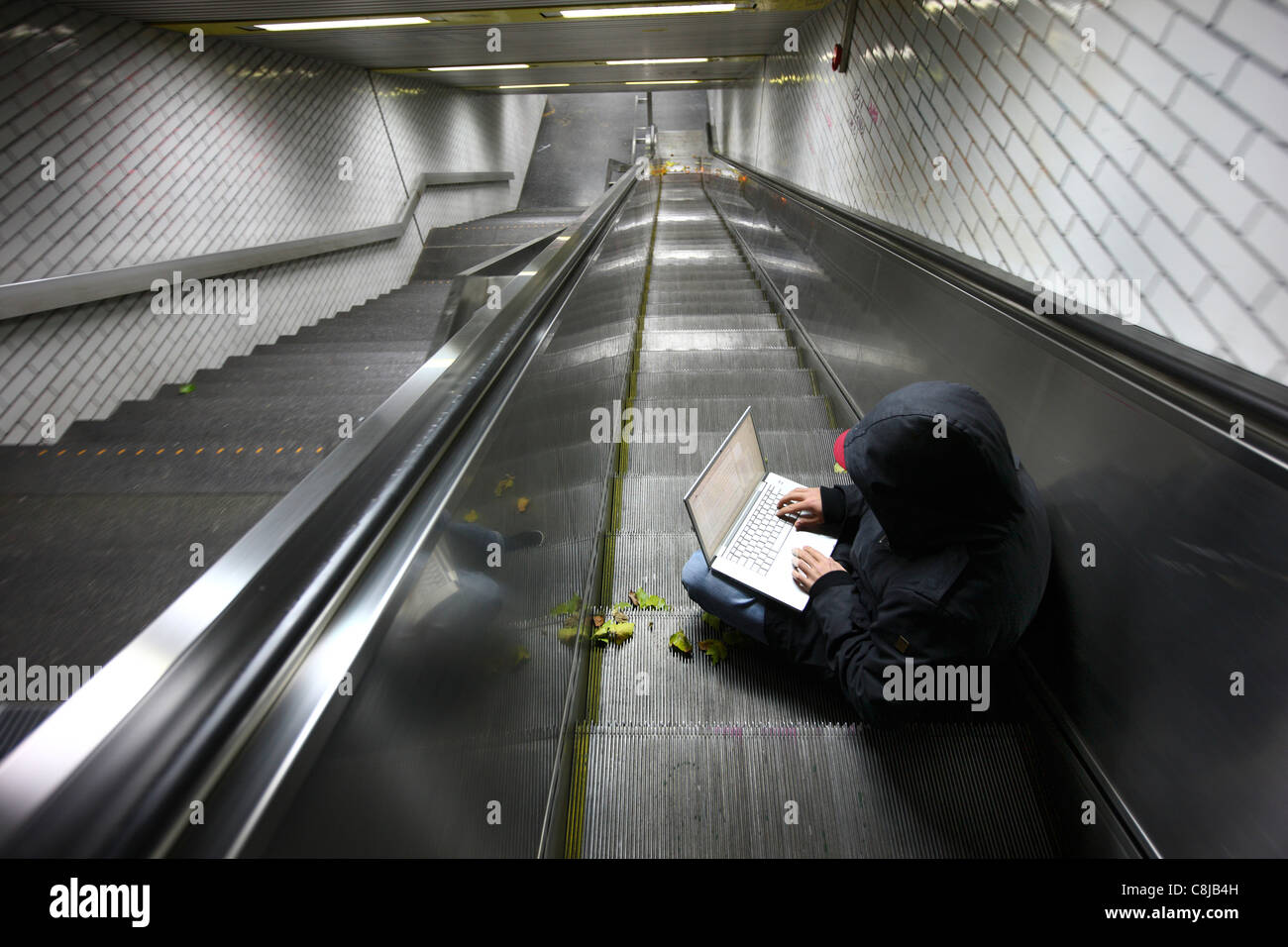 Computer-Benutzer, Hacker, verschwörerisch sitzt mit einem Laptop in einer u-Bahn-Station. Symbolbild, Computer-Internet-Kriminalität. Stockfoto
