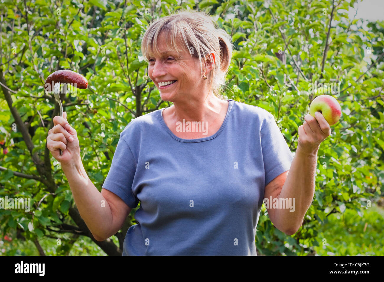 Porträt des mittleren Alter Frau mit Wurst und Apple. Gesunde Lebensweise und Ernährung konzeptionelle Foto. Stockfoto