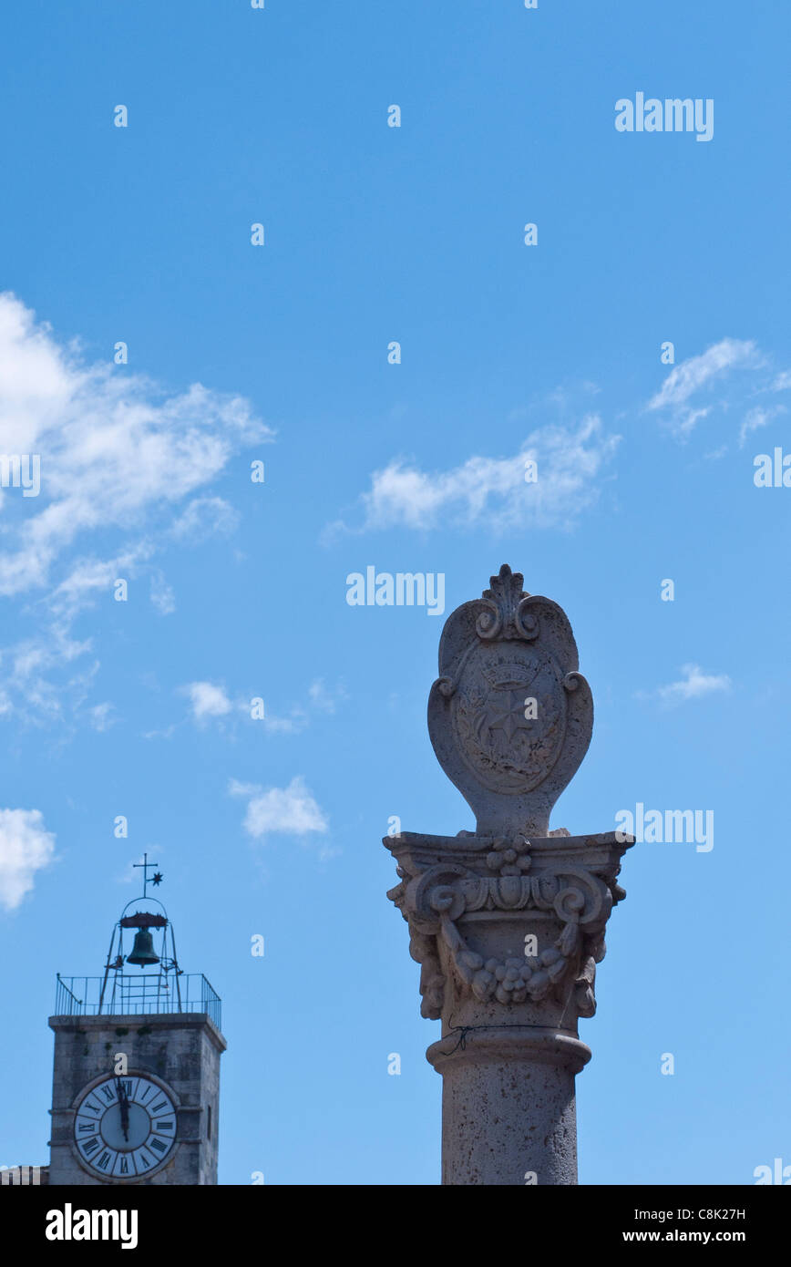 Detail der Spitzen der Denkmal-Spalte im Vordergrund und Uhr/Bell Tower im Hintergrund in Chianciano Terme, Umbrien, Italien. Stockfoto