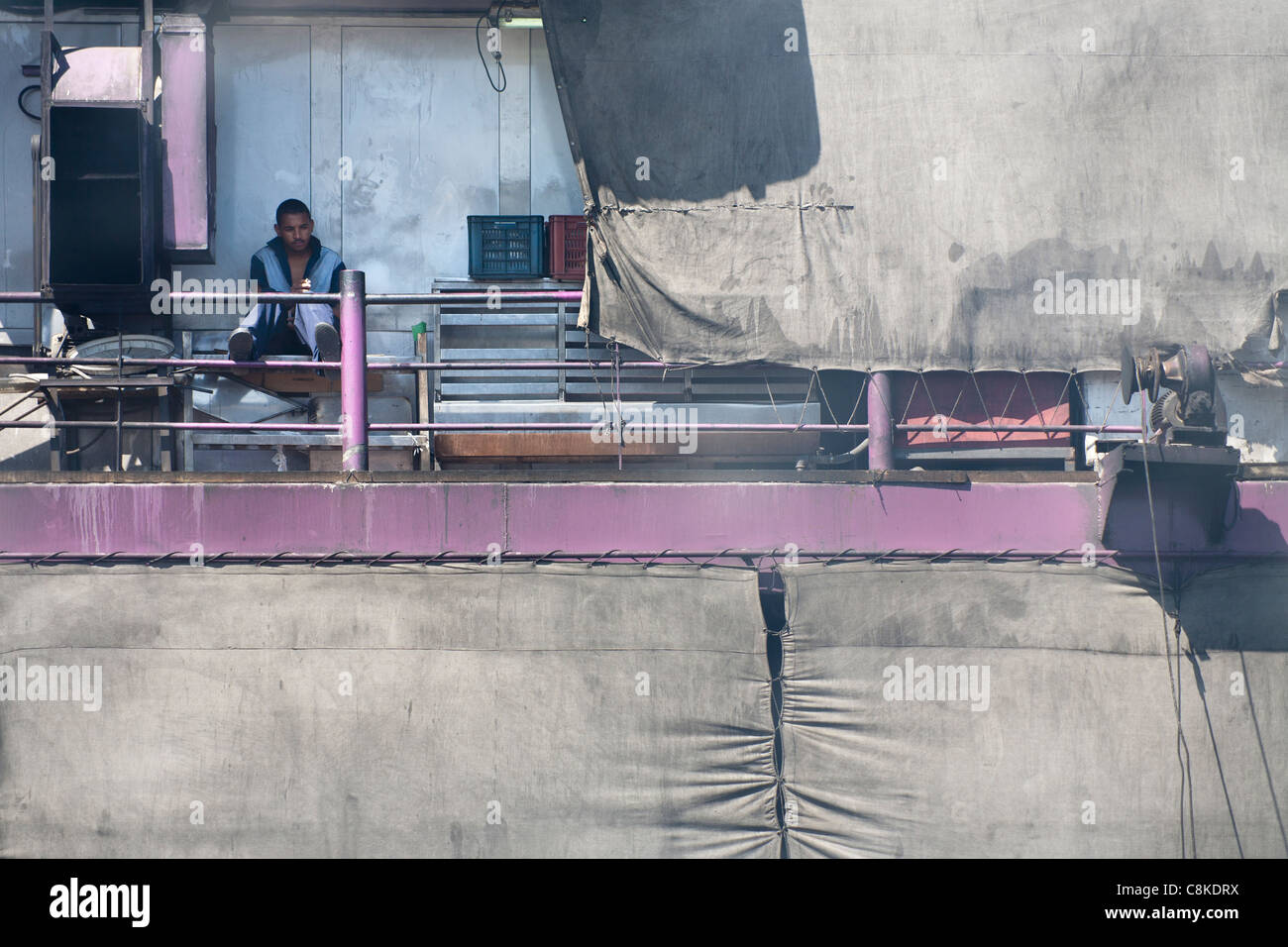 Ein Besatzungsmitglied des Nil Kreuzfahrt Boot sitzen in der rauchigen Dämpfe in das Heck des Schiffes hinter Leinwand-Folie Stockfoto