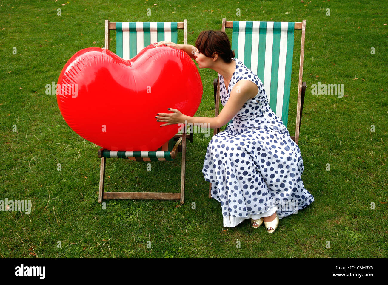 Junge Frau trägt Vintage Kleid sitzt auf einem gestreiften Liegestuhl mit einem großen roten Herz für Unternehmen. Stockfoto