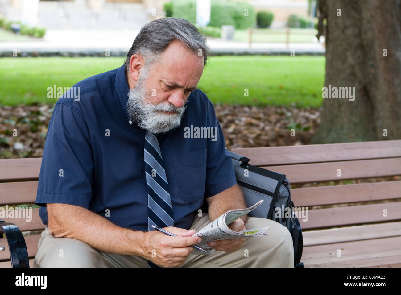 Arbeitsloser Mann mittlerer Alter befasst sich mit Werbung für Arbeitsplätze in einer Zeitung beim Sitzen auf einer Parkbank. Stockfoto