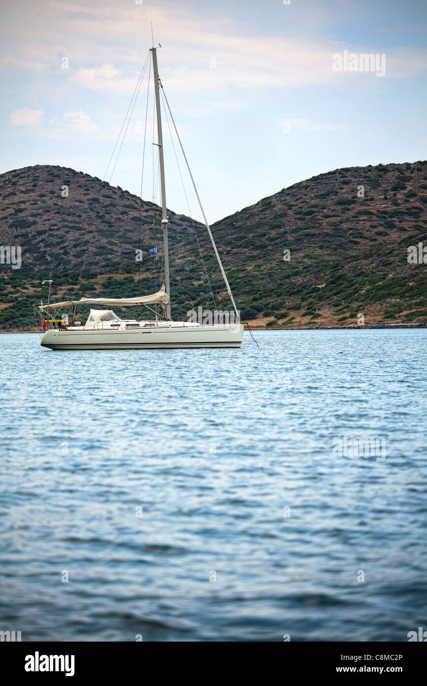 Segelboot am Morgen gegen das Ufer. Vertikale Zusammensetzung. Elounda, Kreta, Griechenland. Stockfoto