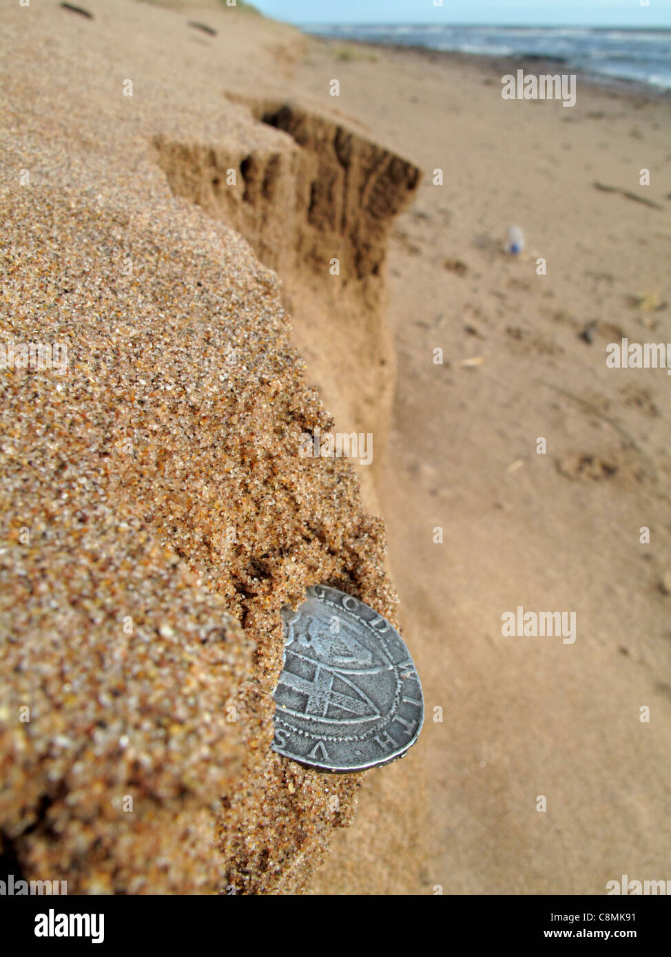 Ein Cromwell Commonwealth Silber Schilling ragt aus einer erodierenden Küsten Sandbank. Stockfoto