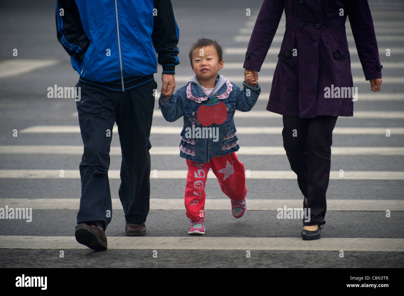 Ein chinesisches Mädchen hält Elternteils Hände überqueren einer Straße in Peking, China. 20. Oktober 2011 Stockfoto