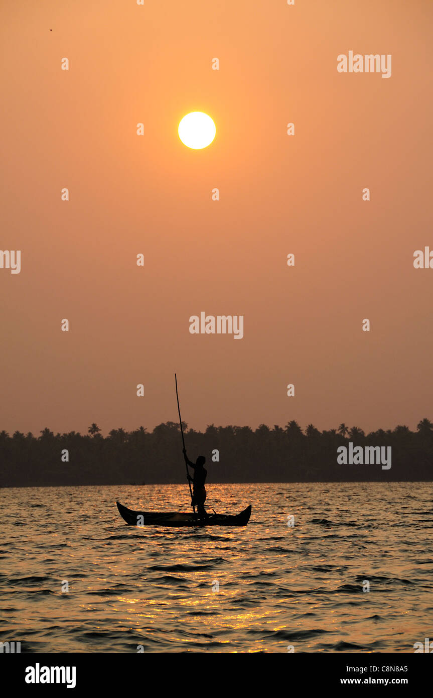 Vertikale Schuss des Sonnenuntergangs am Vembanad See, Kerala, Indien, mit Fährmann Stechkahn fahren seine Holzboot über den See im Vordergrund Stockfoto
