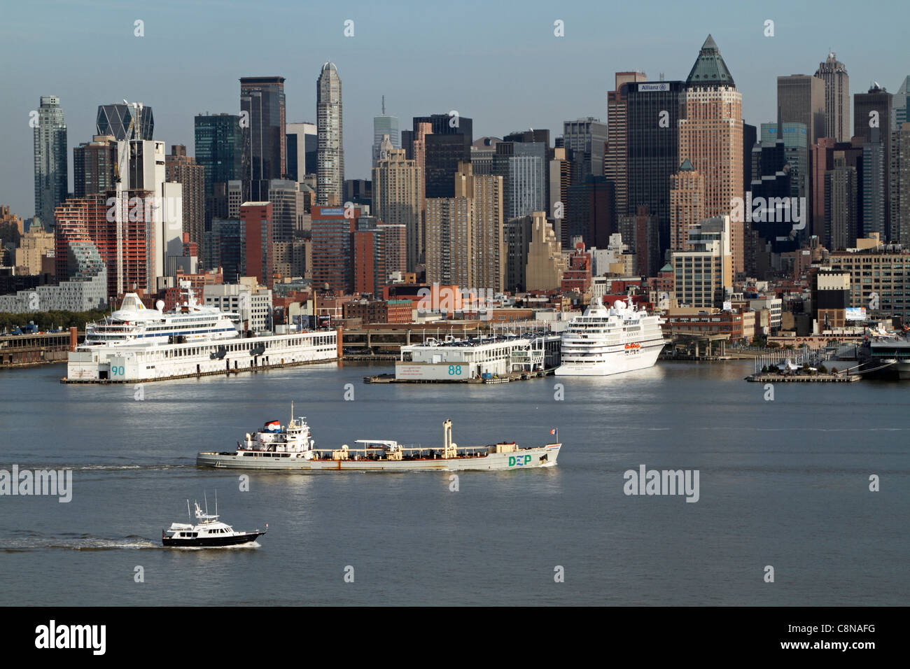 Boote auf dem Hudson River, die an angedockten Kreuzfahrtschiffen vorbeifahren. Das Boot in der Mitte des Flusses ist ein Schlammboot. Stockfoto