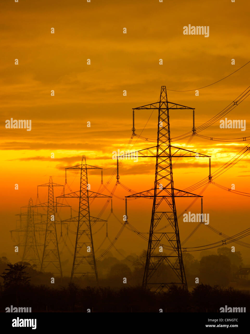 Eine Reihe von Strommasten gegen einen orangefarbenen Himmel Stockfoto