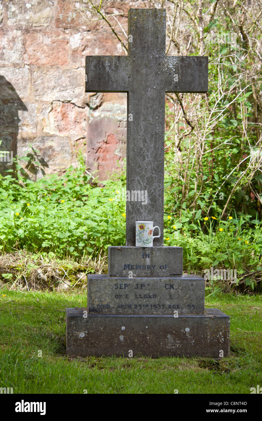 Ein Kruzifix Grabstein im Friedhof mit einer Tasse Tee auf der unteren Leiste links Stockfoto