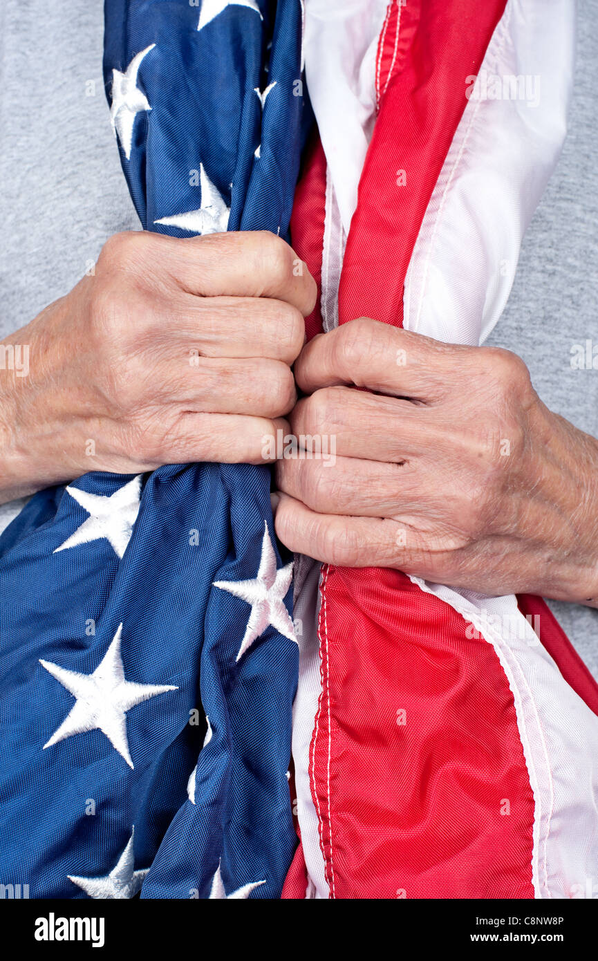 Eine ältere patriotische Frau umklammert eine amerikanische Flagge, um ihren Hals drapiert. Stockfoto
