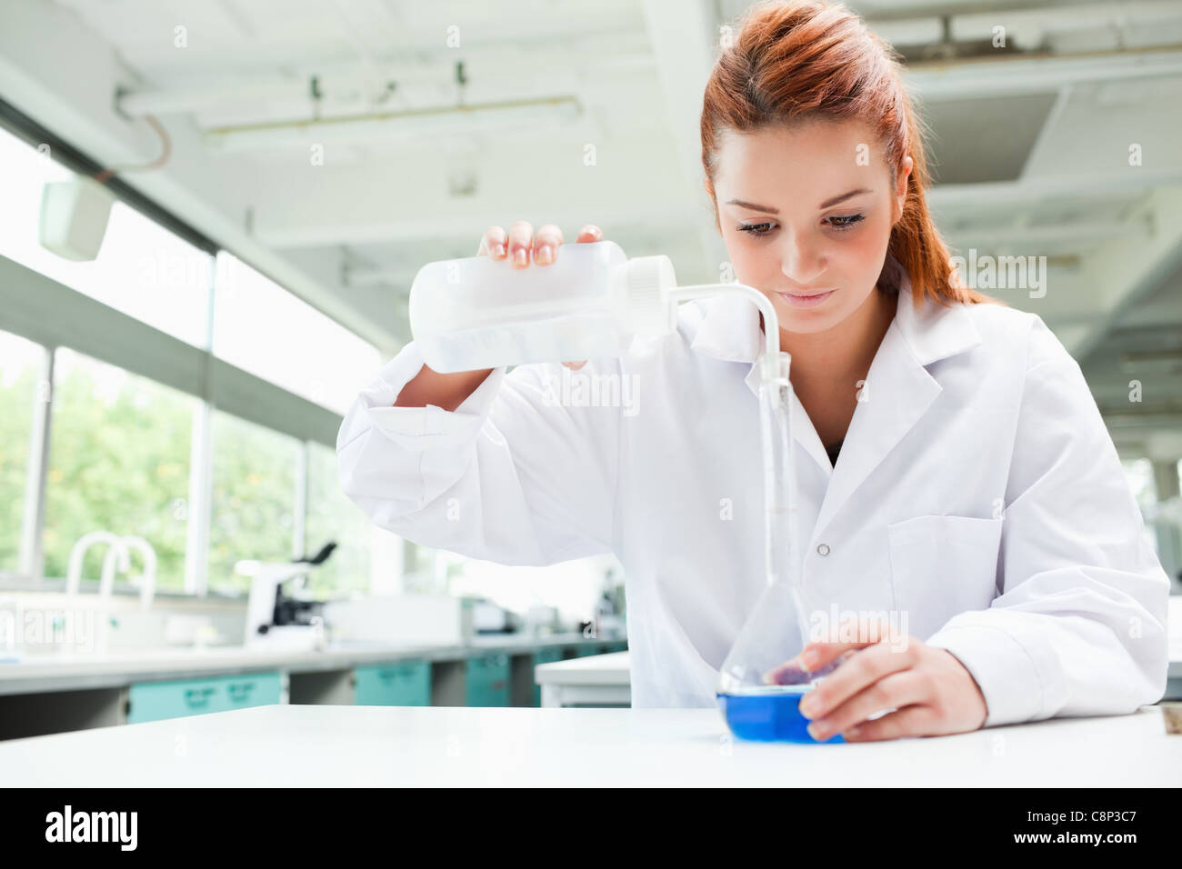 Rothaarige fokussierte Wissenschaftler Flüssigkeit in eine Flasche gießen Stockfoto