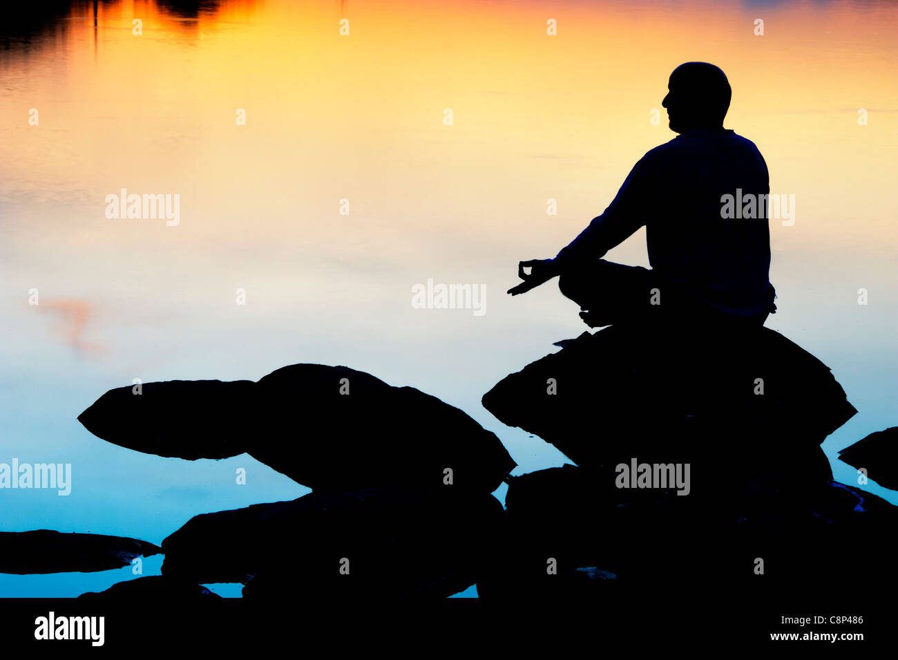 Sunrise Silhouette eines Mannes über Felsen an einem indischen See zu meditieren. Andhra Pradesh, Indien Stockfoto