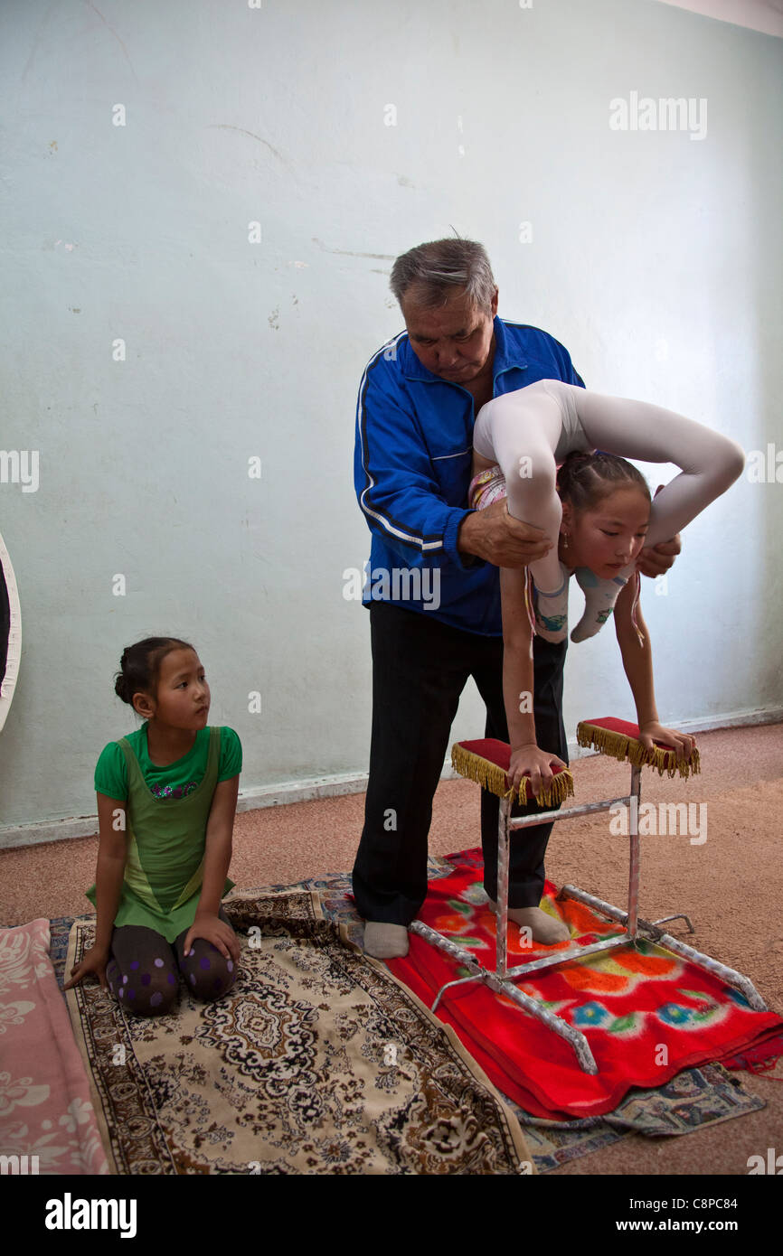 Trainer helfen jungen Schlangenmensch Mädchen mit ihre Beine über den Kopf, während ein anderes Mädchen blickt auf Stockfoto