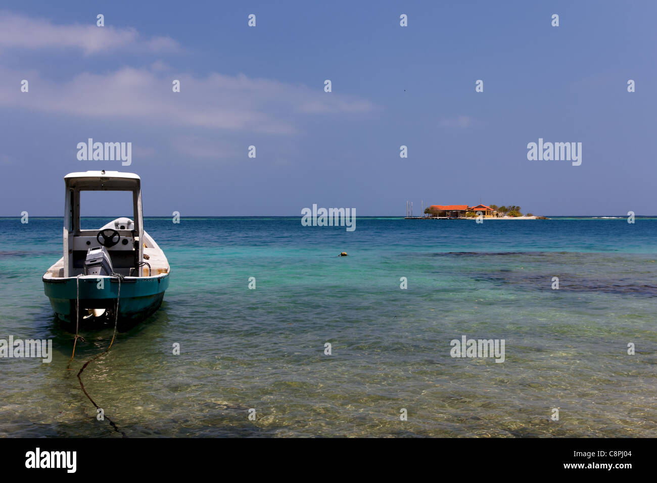 Ein kleines Boot verankert im Vordergrund, mit einer kleinen karibischen Insel im Hintergrund sichtbar. Stockfoto