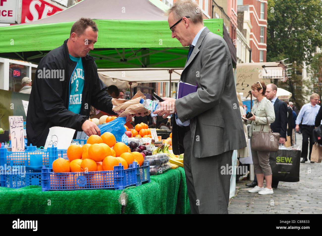 Ein Geschäftsmann im Anzug kauft frisches Obst aus Obst und Gemüse Stand auf einem Markt in Victoria, London 2011 Stockfoto