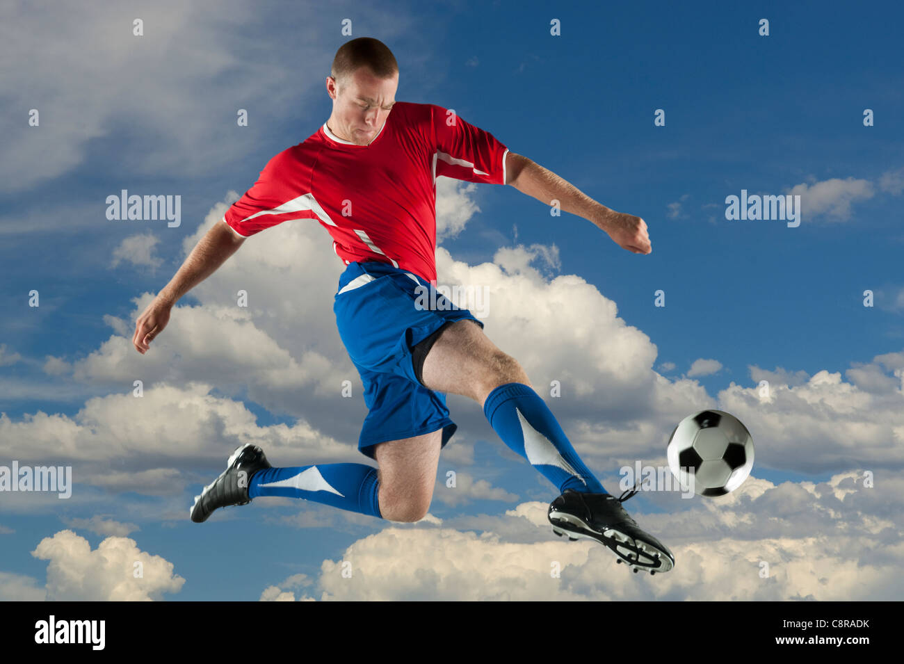 Kaukasische Fußballspieler springen in der Luft treten Kugel Stockfoto