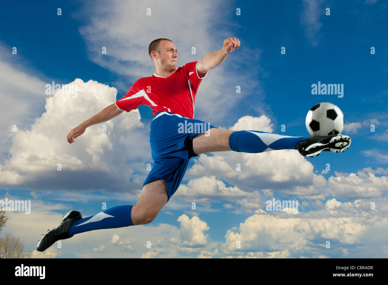 Kaukasische Fußballspieler springen in der Luft treten Kugel Stockfoto