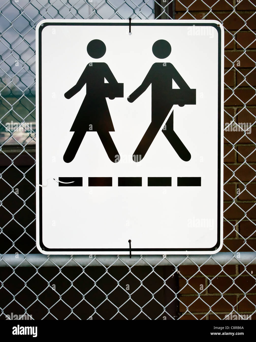 Ein Schild an einem Ketteverbindung Zaun zeigt Symbole für Mann und Frau zu Fuß mit gedrückter Aktentaschen. Stockfoto