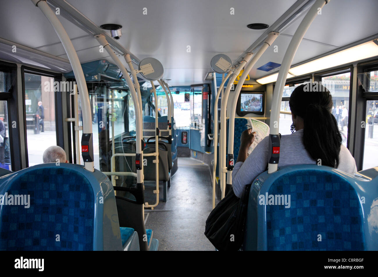 Innenraum des öffentlichen Nahverkehrs Eindeckbus & Passagiere sitzen innen Rückansicht Frau, die Sicherheit CCTV-Bildschirm vor London England Großbritannien ansieht Stockfoto