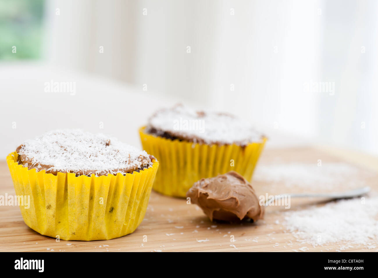 Zwei Schokoladen Cupcakes mit Kokosnuss auf Schneidebrett mit Löffel und Puderzucker bestreut. Stockfoto
