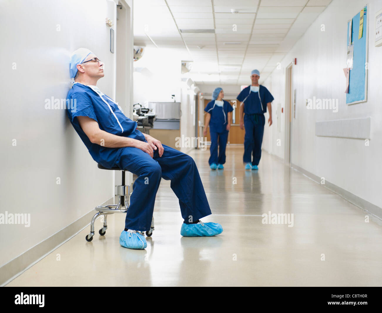 USA, Utah, Ogden, Chirurg im Krankenhausflur nach Operation, ruhen, während zwei seiner Kollegen im Hintergrund laufen Stockfoto