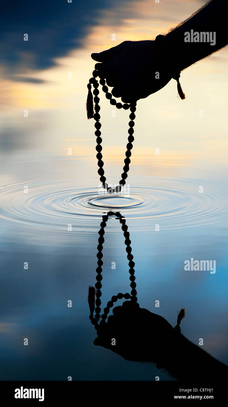 Hand, die indischen Rudraksha / Japa Mala Gebet Perlen über Plätschern des Wassers. Silhouette Stockfoto