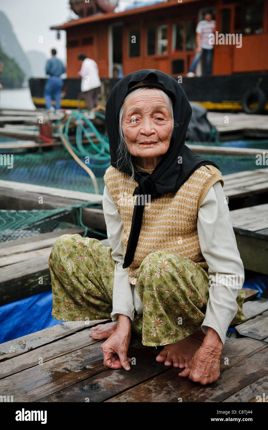 Eine ältere vietnamesische Frau sitzt auf einem Angelpier in der Halong Bay Stockfoto