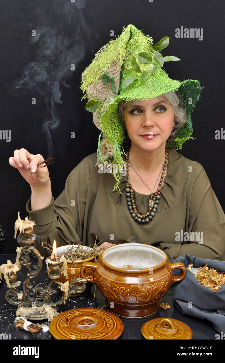 Magische Frau im grünen Hut mit Rauchen Zweige auf schwarzem Hintergrund Stockfoto