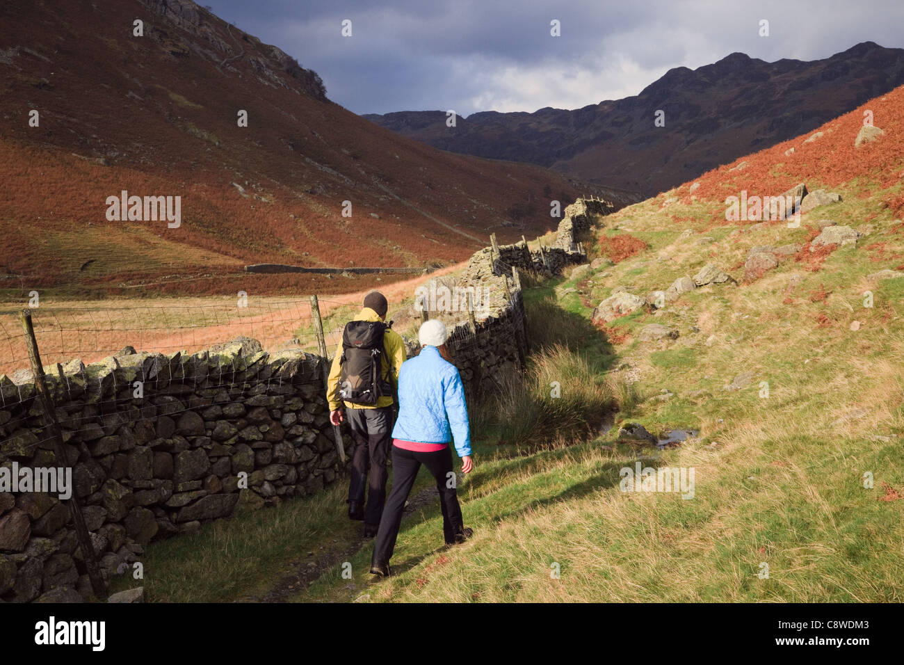 Zwei Menschen wandern auf Cumbria Weg neben einem trockenmauern Wand durch Langstrath Tal in Hills Lake District National Park Cumbria England Großbritannien Großbritannien Stockfoto