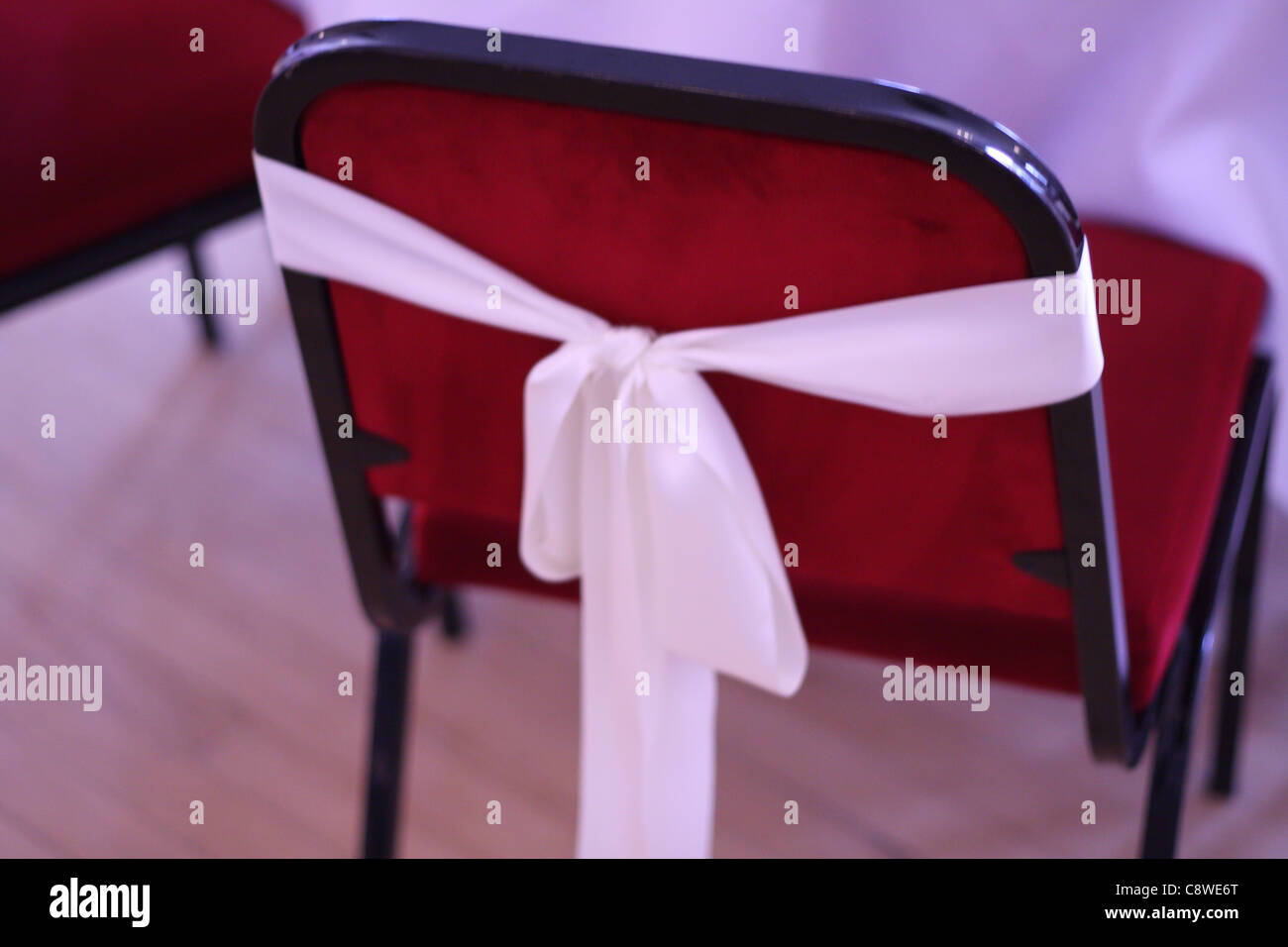 Ein weißer Seide oder satin Stoff Bogen um jeden roten Stuhl auf eine zivile Trauung gebunden Stockfoto