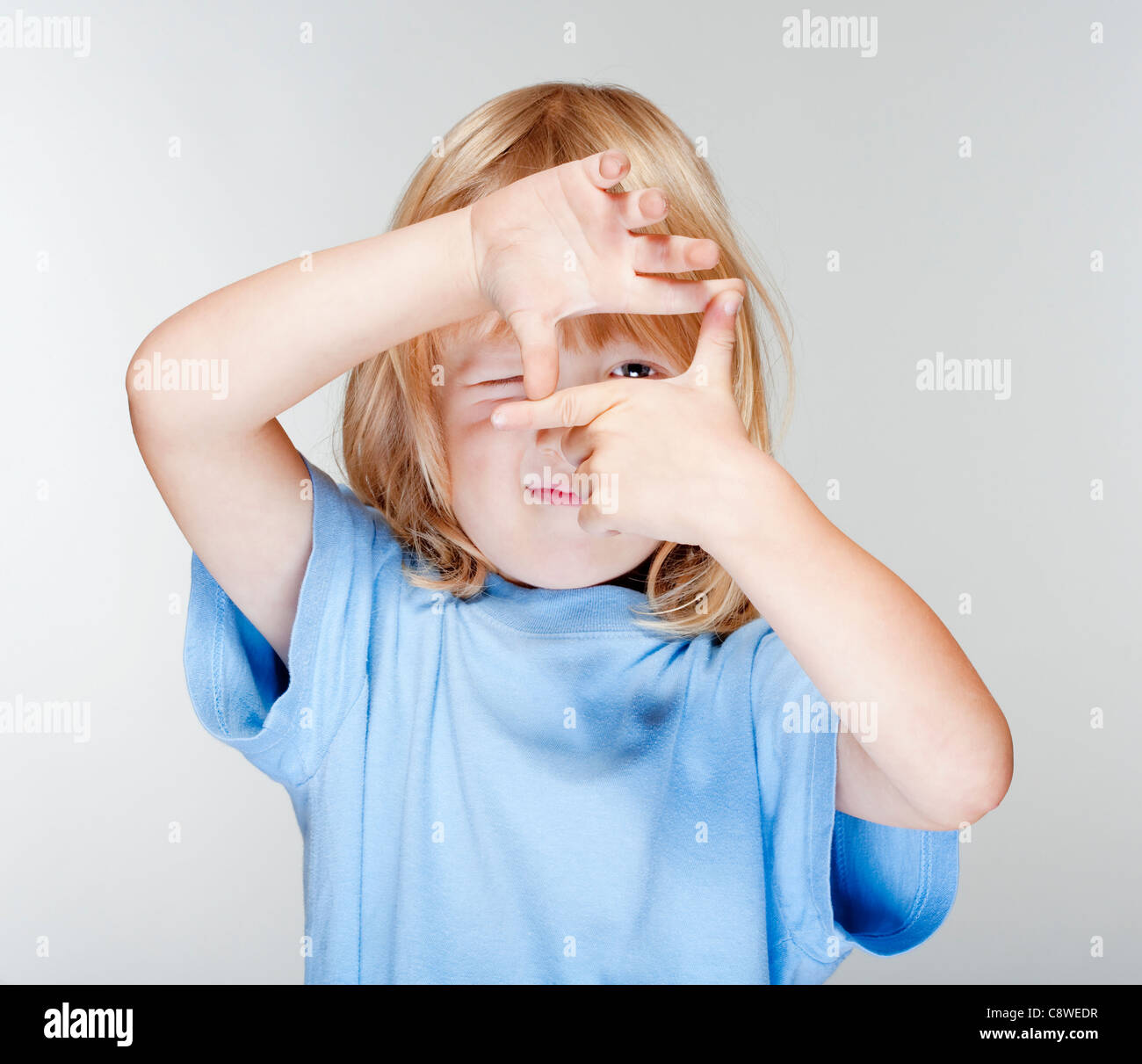 kleiner Junge mit langen blonden Haaren, die durch einen Finger Frame - isoliert auf grau Stockfoto